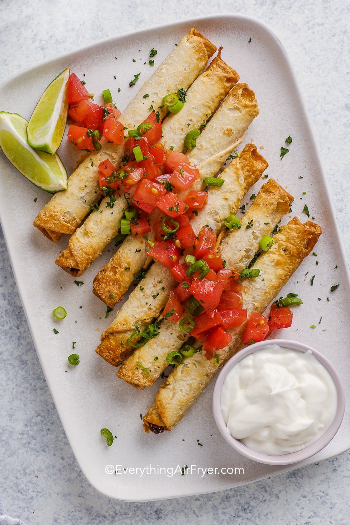 taquitos on a plate with sour cream and tomatoes
