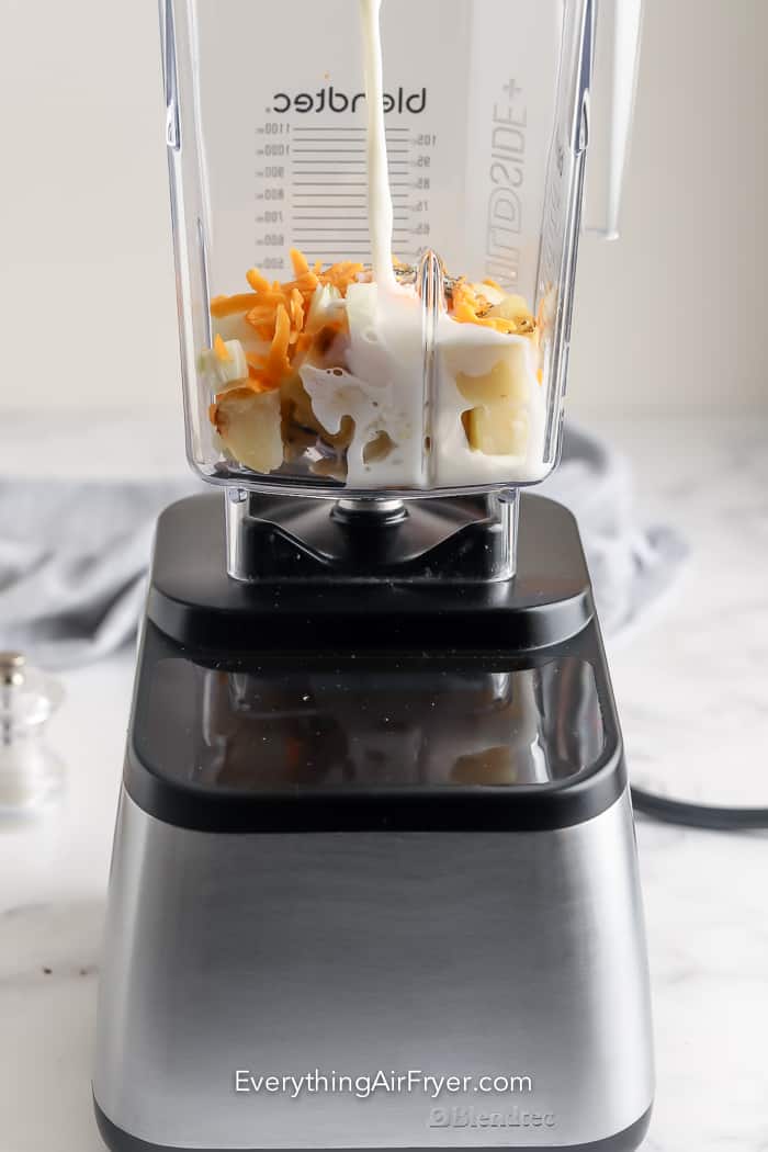 Milk being poured on cheesy potato soup ingredients in a blender