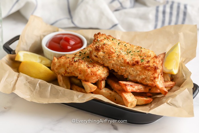 fish and chips in a basket with ketchup and lemon wedges