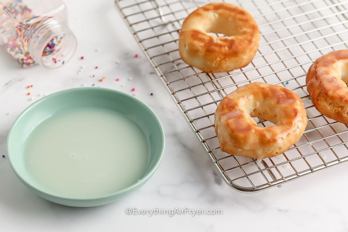 donuts on a drying rack next to a bowl of glaze