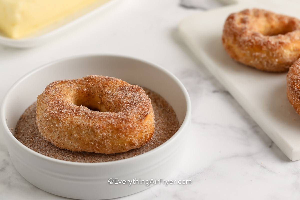 Cooked donuts being rolled in cinnamon sugar