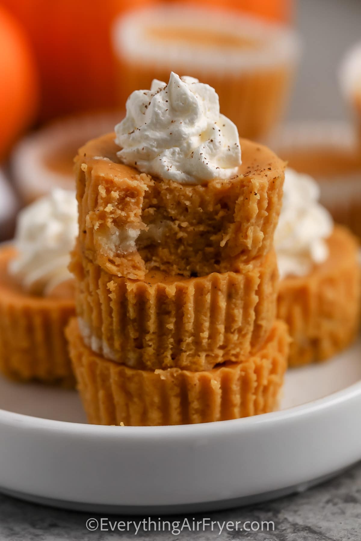 A stack of mini pumpkin cheesecakes topped with whip cream