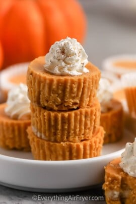 Three mini pumpkin cheesecakes stacked on a plate and topped with whip cream