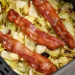 Chopped cabbage topped with bacon in an air fryer basket with writing