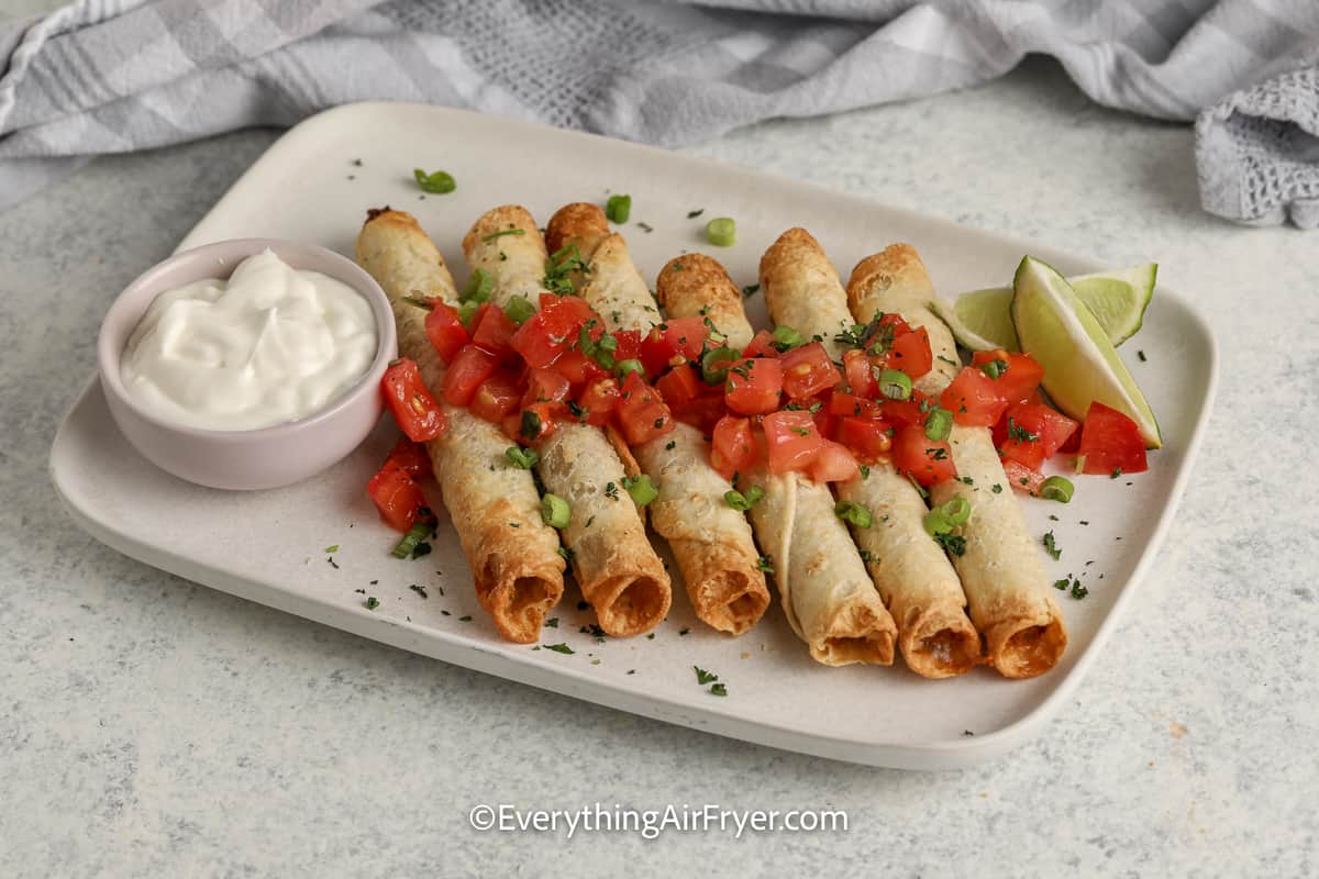 cooked taquitos on a plate topped with tomatoes