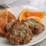 sausage patties on a plate with toast and orange slices