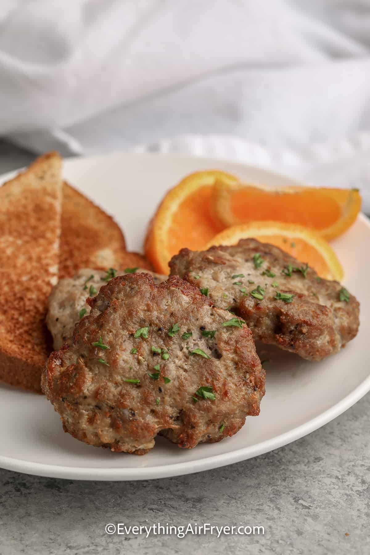 sausage patties on a plate with toast and orange slices
