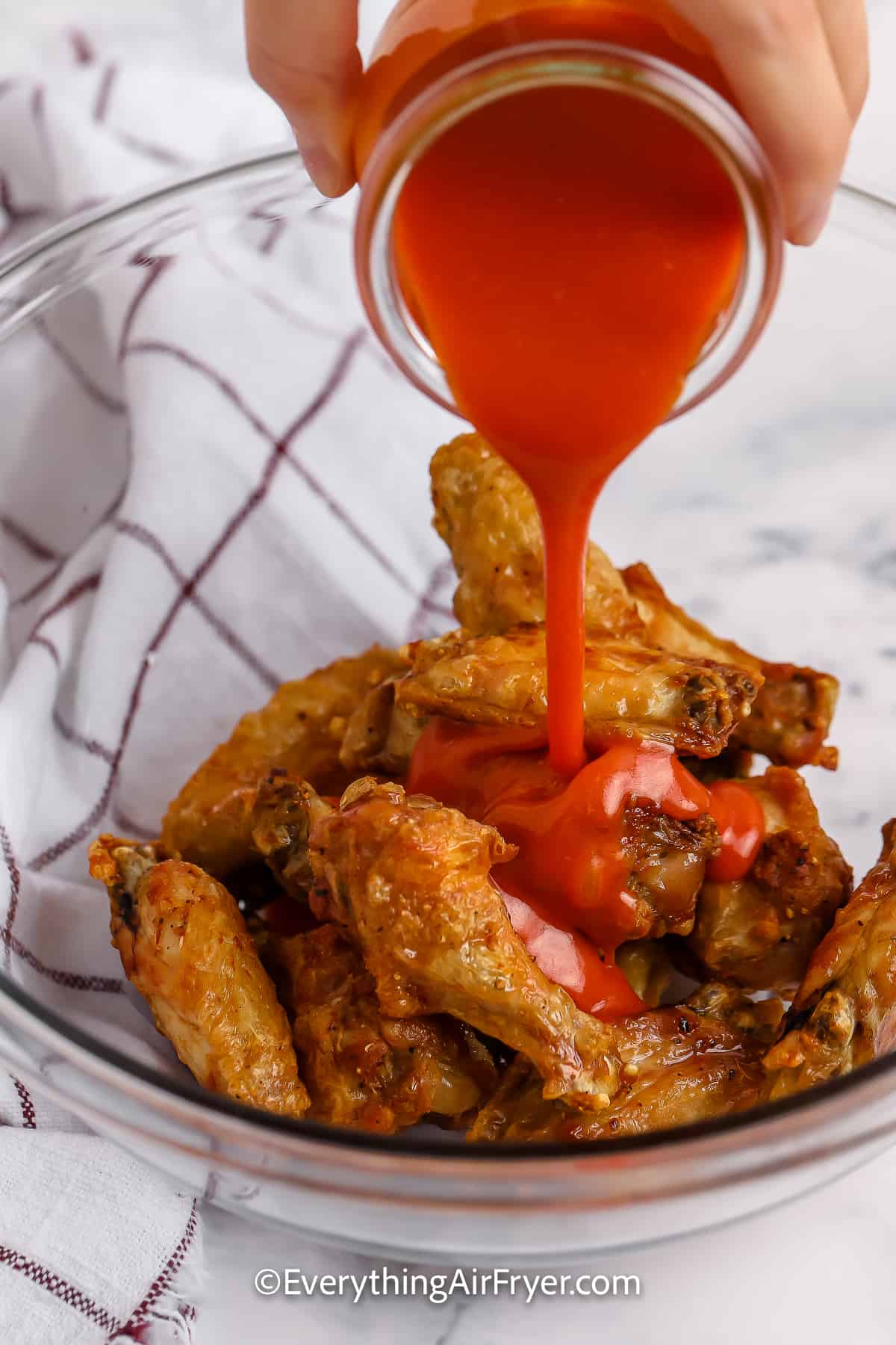 Buffalo sauce being poured over cooked chicken wings