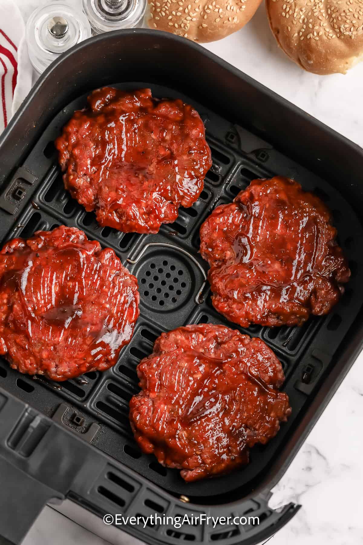 uncooked hamburger patties in an air fryer tray