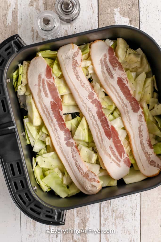 Chopped Cabbage in an air fryer basket topped with bacon
