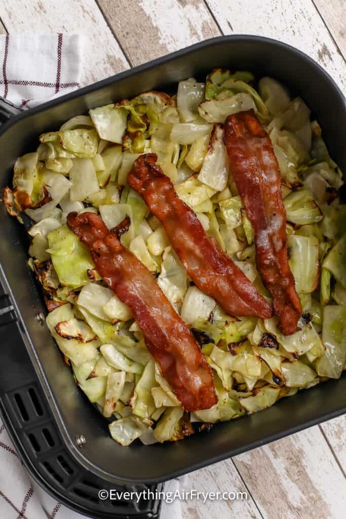 Cooked cabbage topped with bacon in an air fryer basket