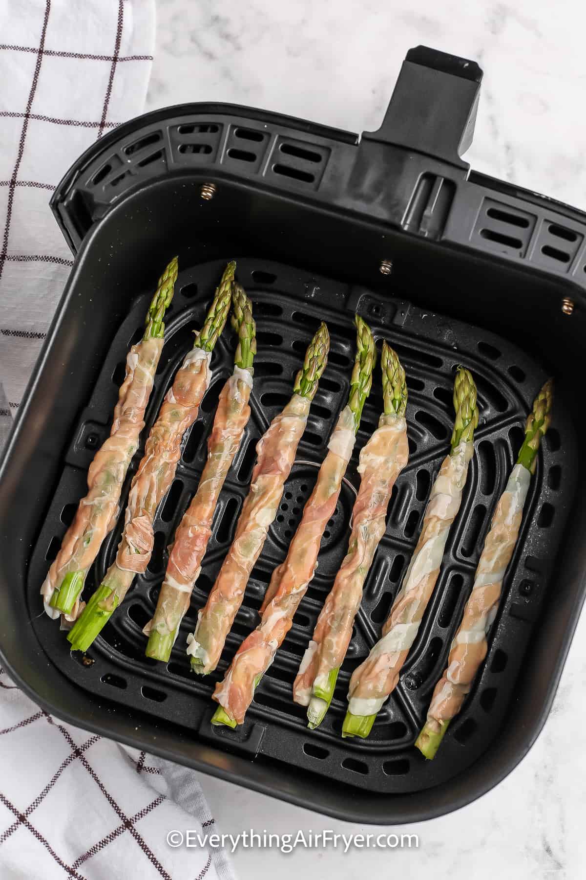 Prosciutto wrapped asparagus prepped in an air fryer basket