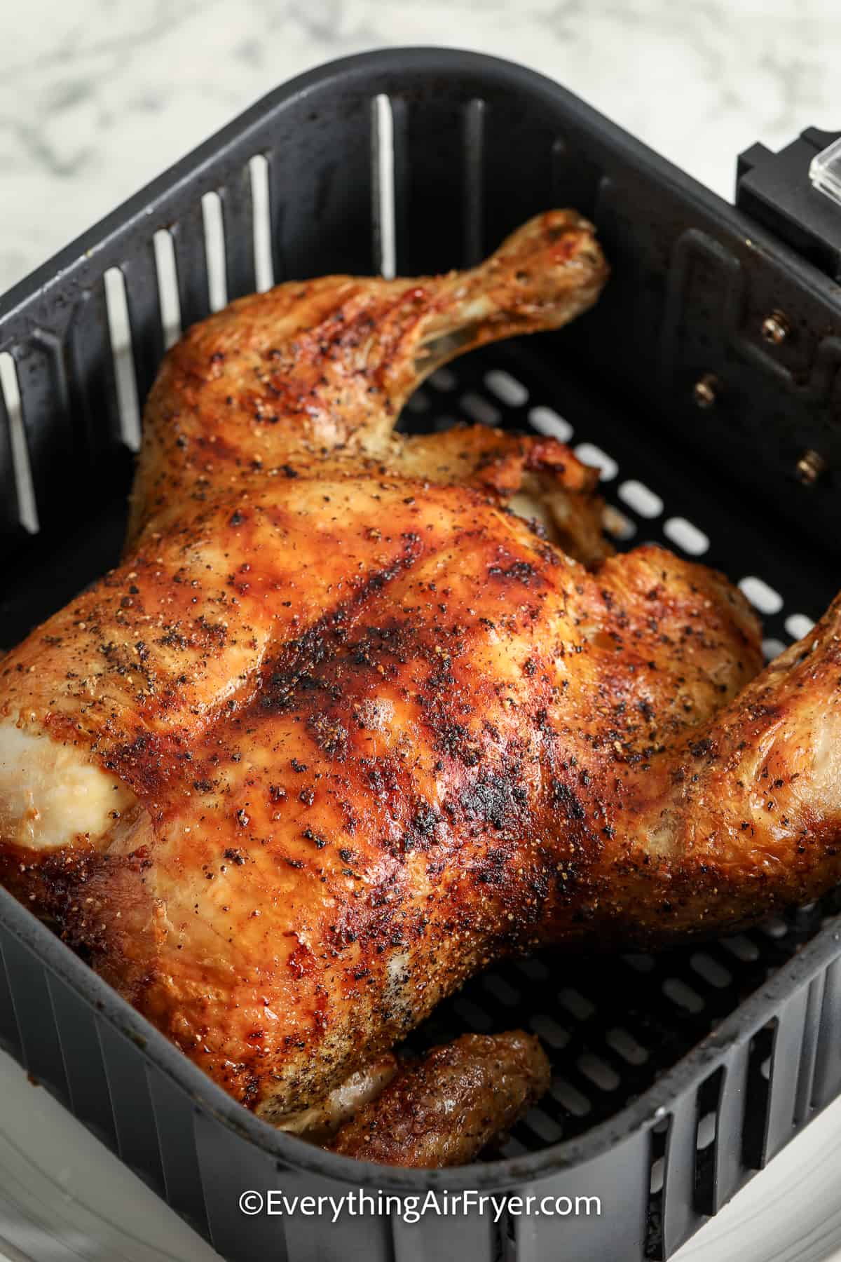 Cooked whole chicken in an air fryer basket