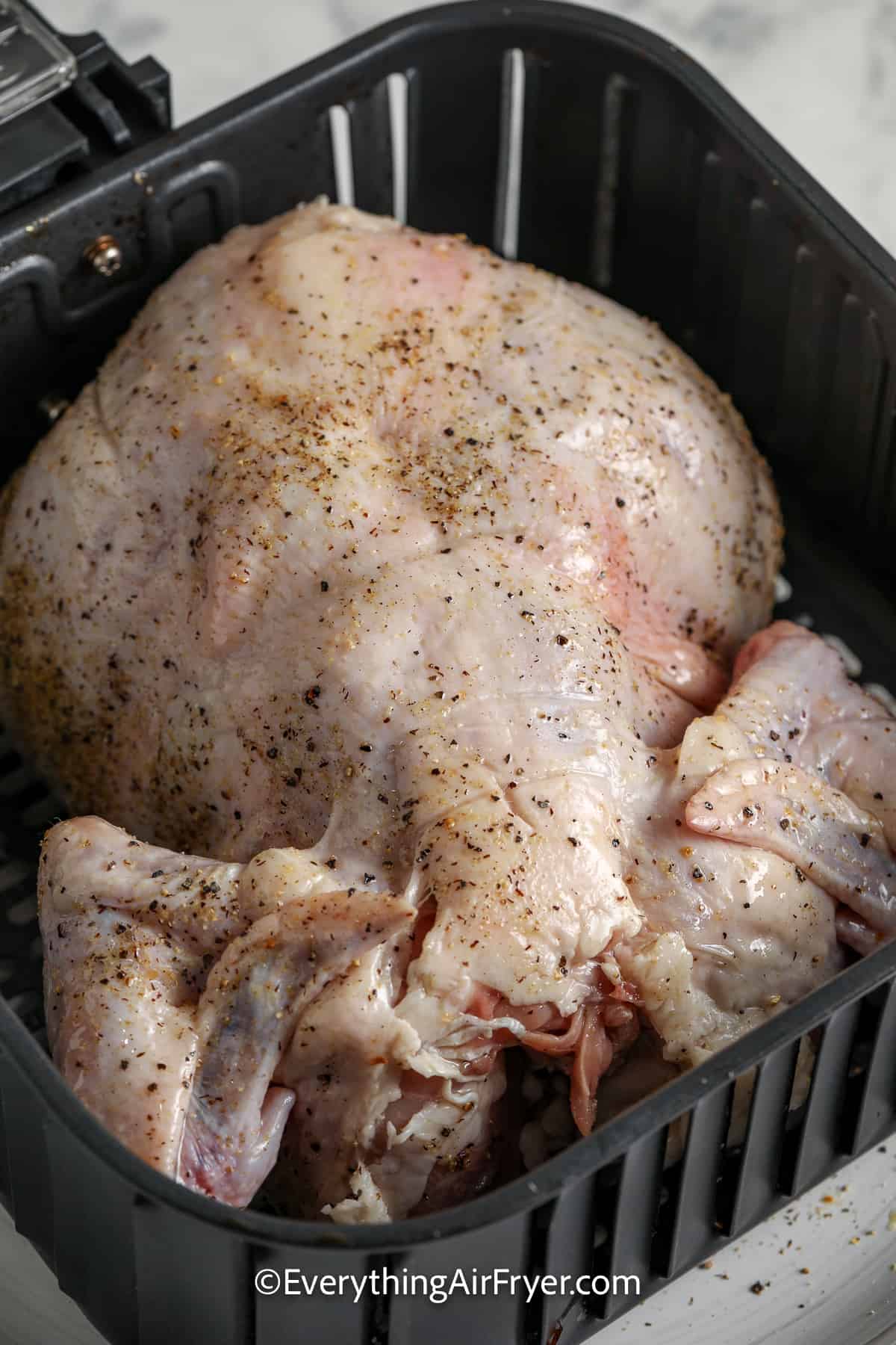 raw whole chicken with seasoning in an air fryer basket