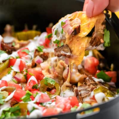 hand pulling nacho chip from an air fryer tray