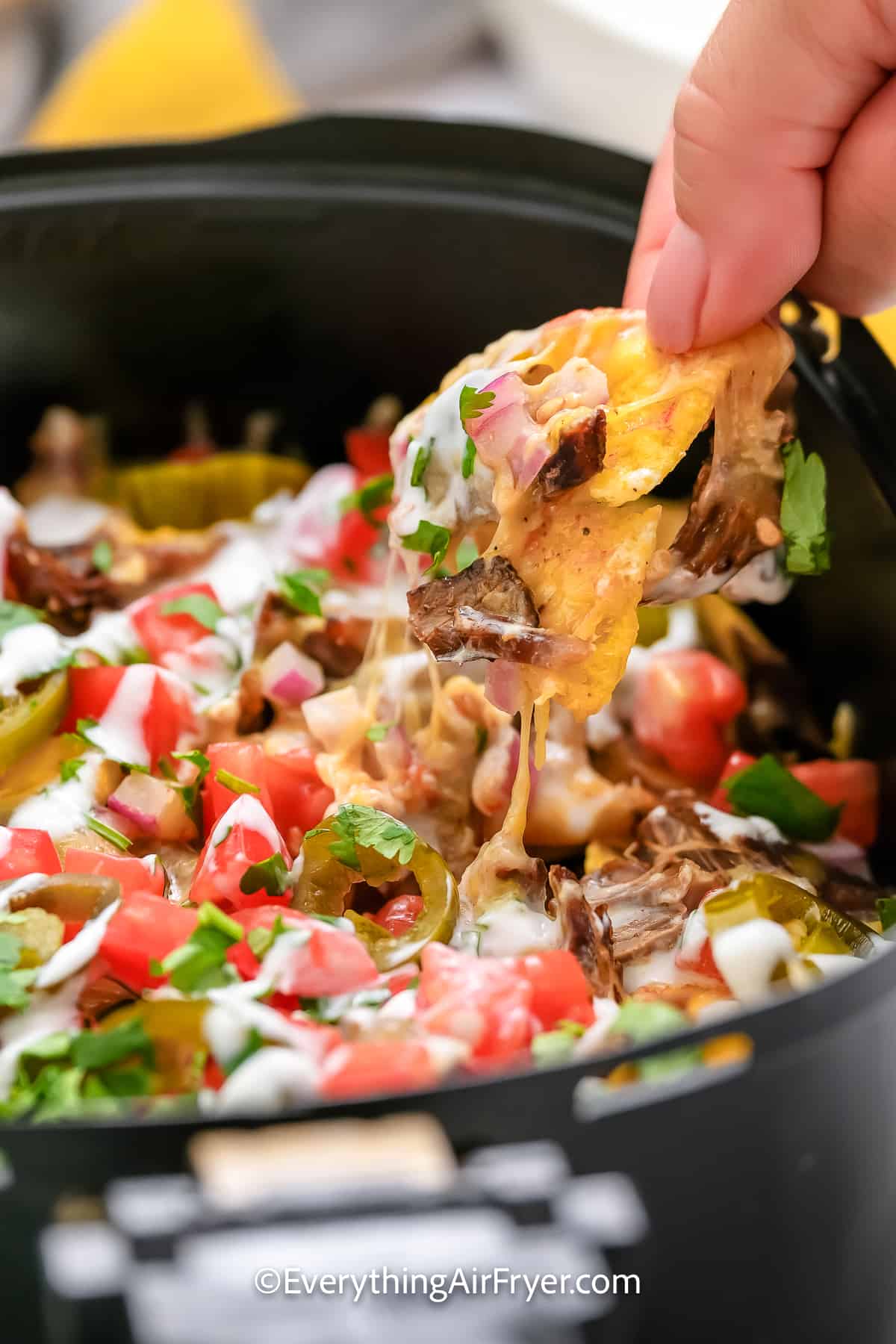 hand pulling nacho chip from an air fryer tray
