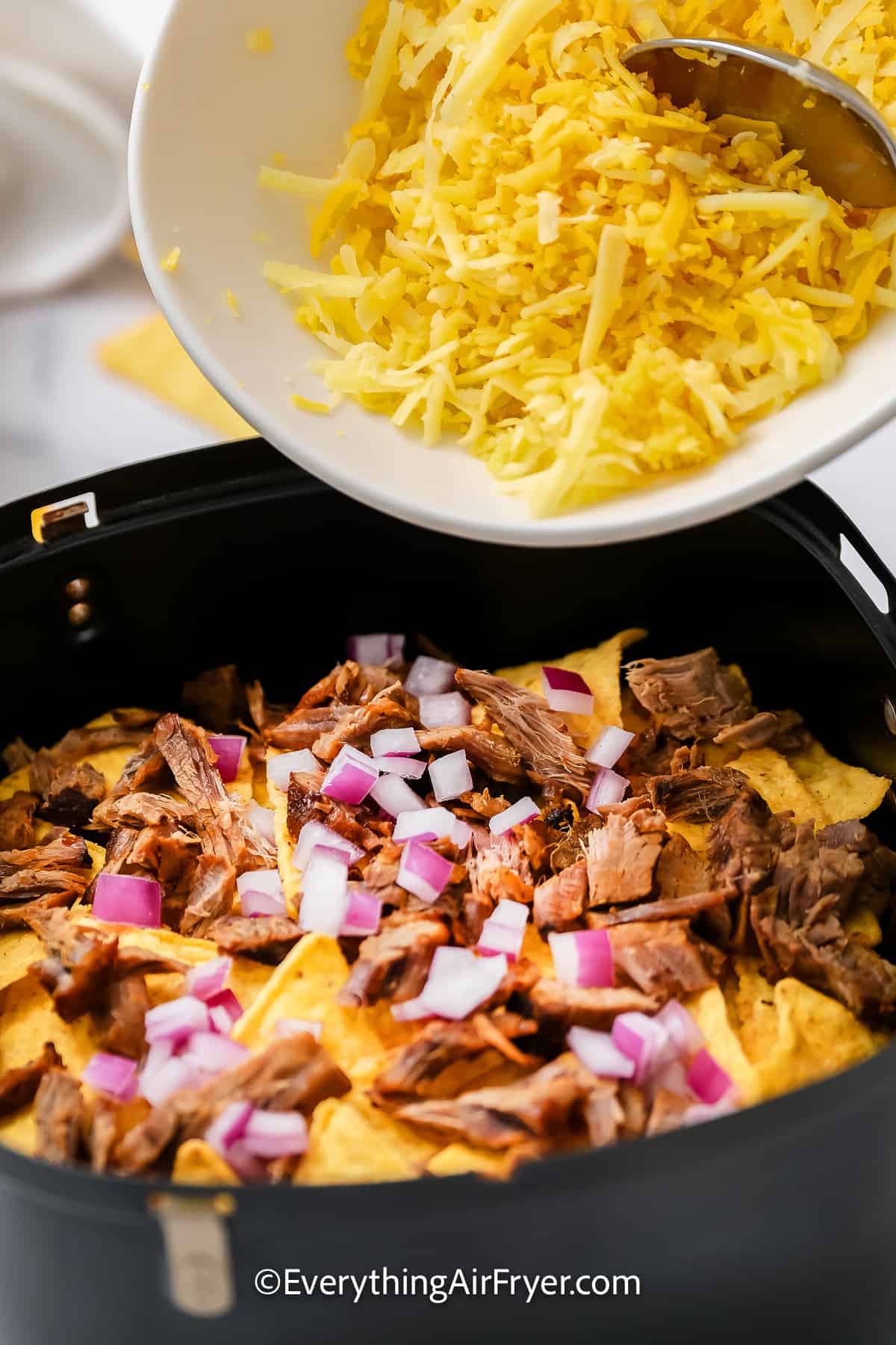 dumping grated cheese onto nacho chips in an air fryer tray