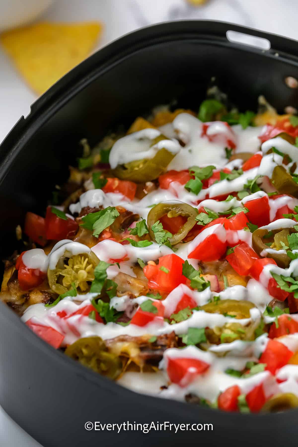 nachos layered with cheese, brisket, jalapeños, and tomatoes in an air fryer tray