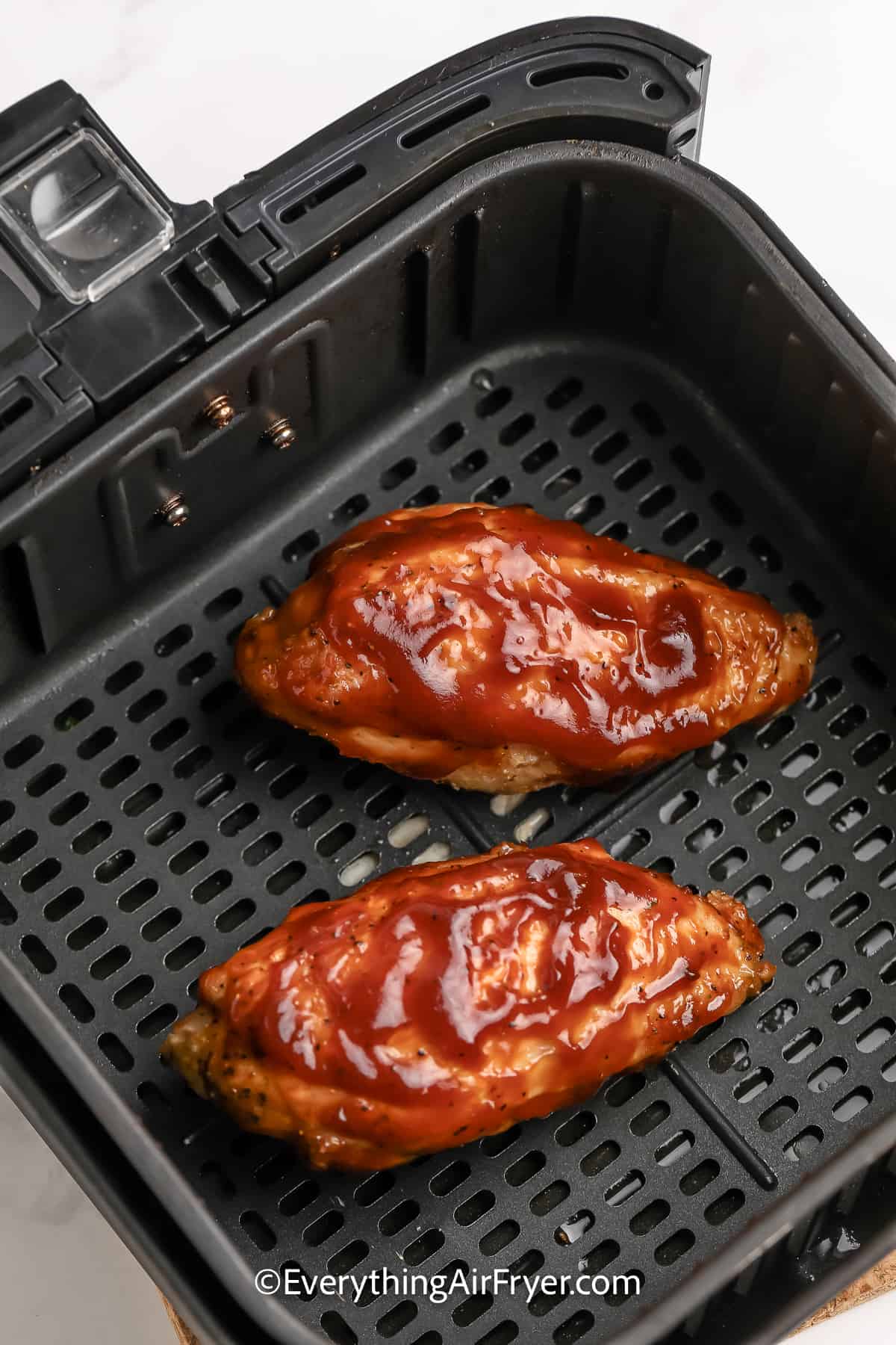 uncooked chicken breasts covered in bbq sauce in an air fryer tray