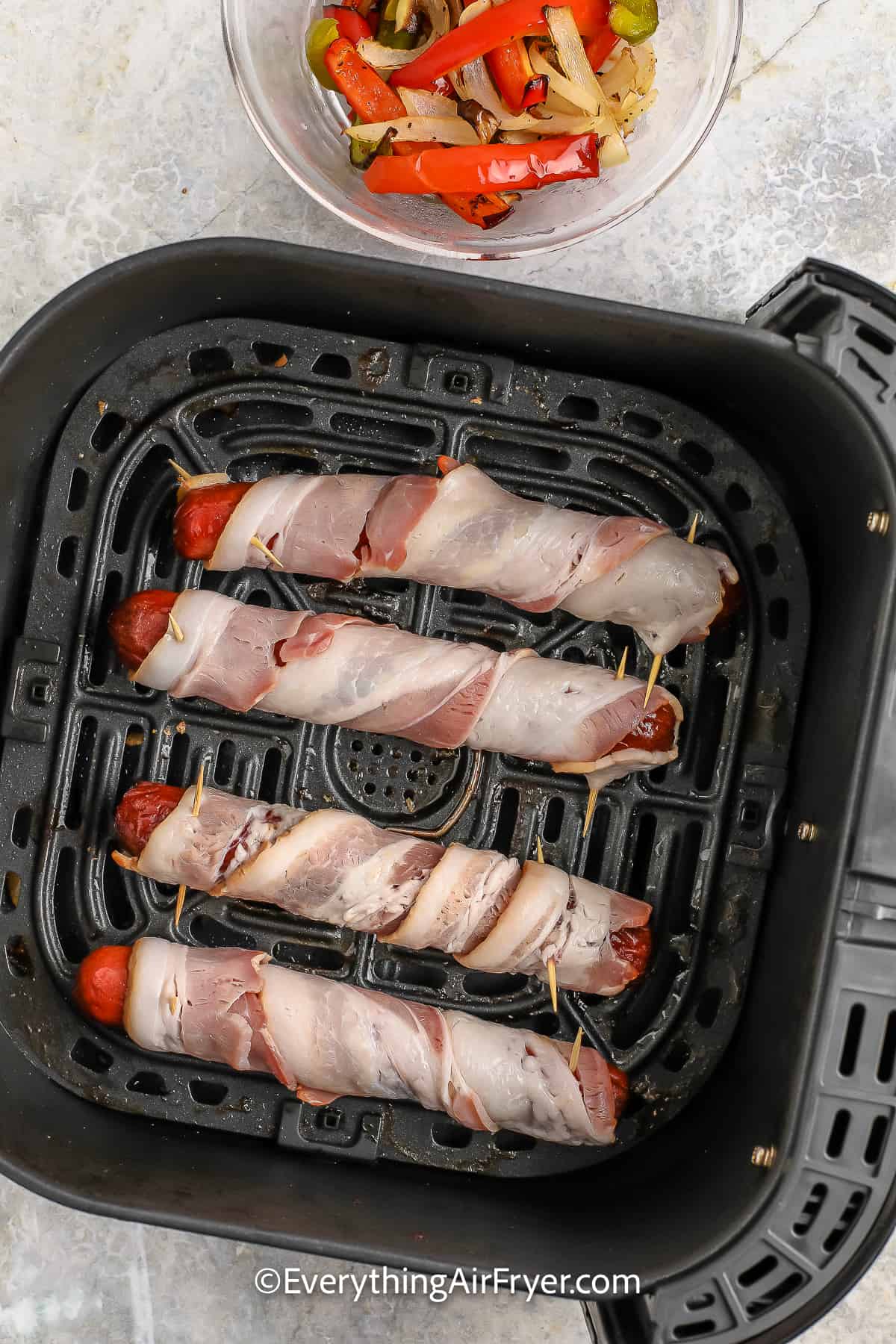 Hot dogs wrapped in bacon in an air fryer basket