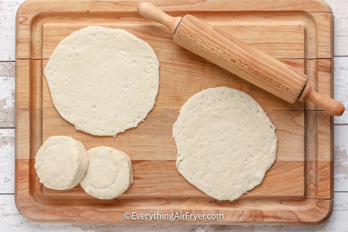 Biscuit crust for a breakfast pizza being rolled out on a cutting board