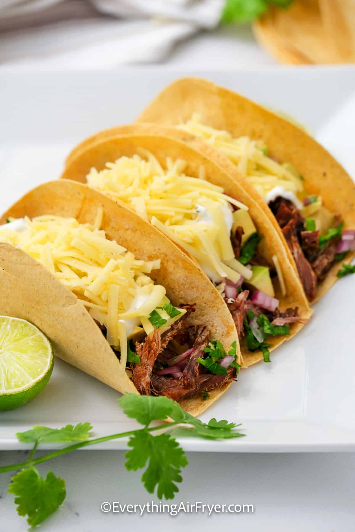 Three Air Fryer Brisket Tacos on a plate with cilantro and limes