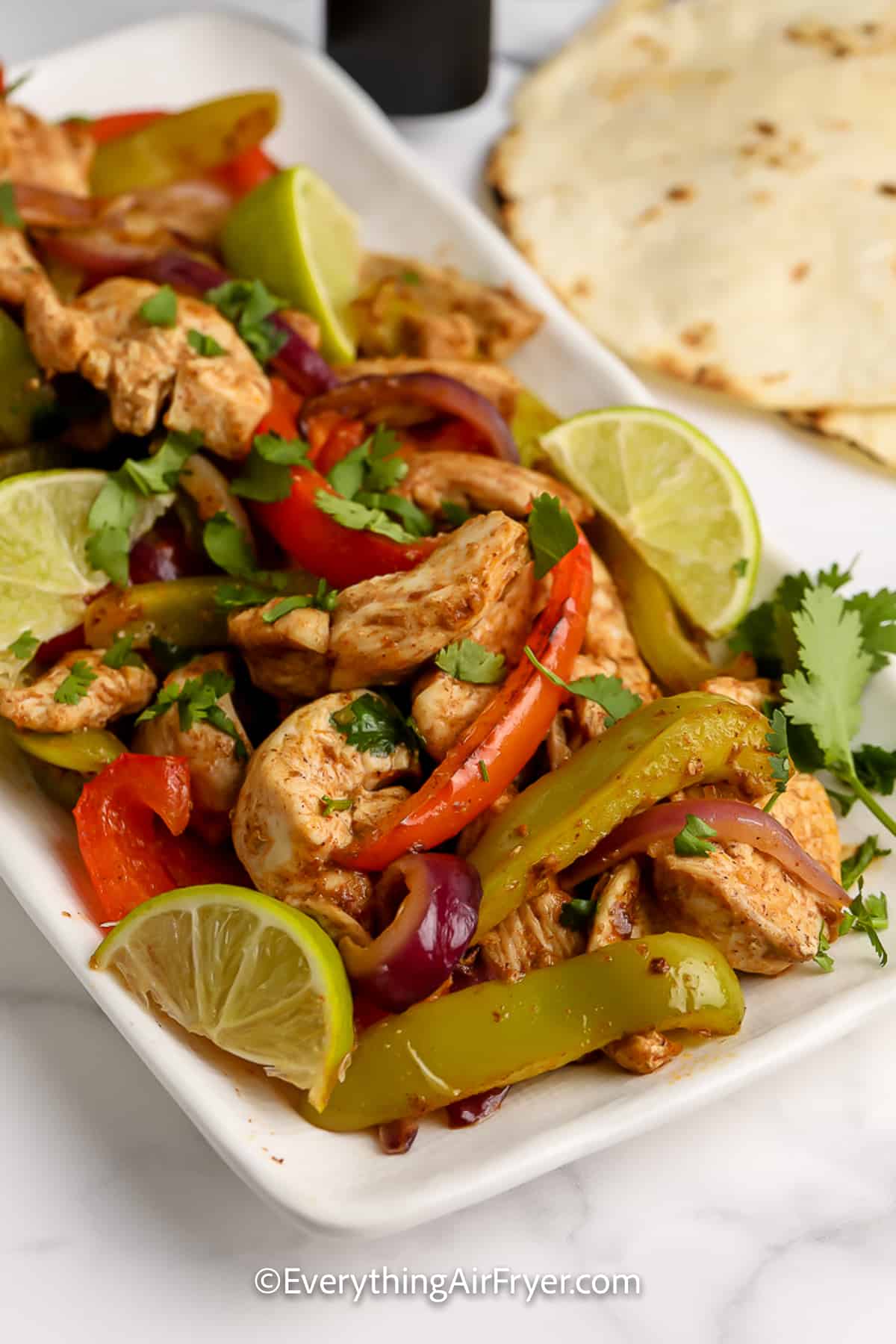 A serving platter of Air Fryer Chicken Fajitas Ingredients with lime wedges