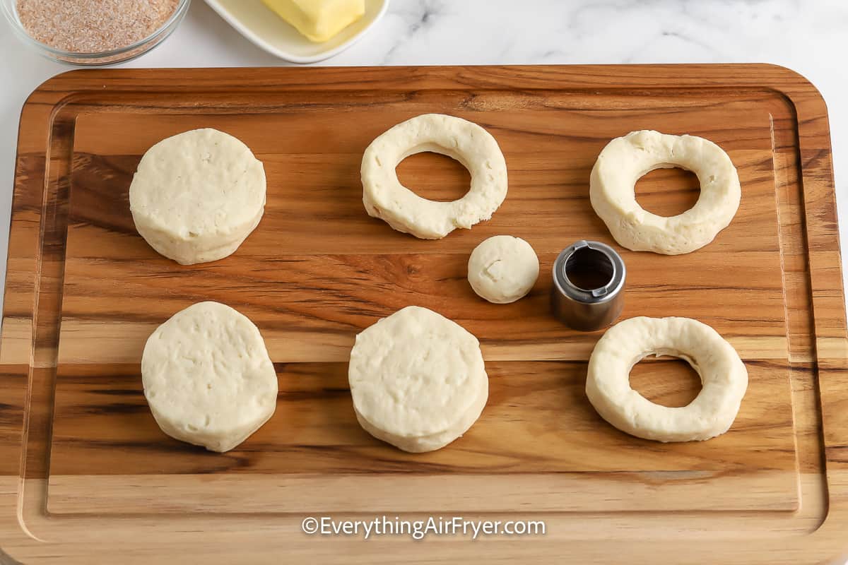 refrigerator biscuits on a cutting board with the centres punches out.
