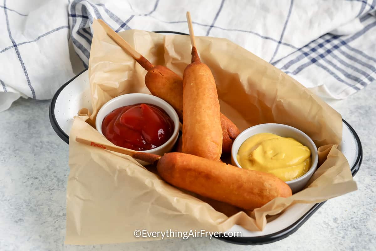 A serving dish with three air fryer corn dogs and ketchup and mustard.