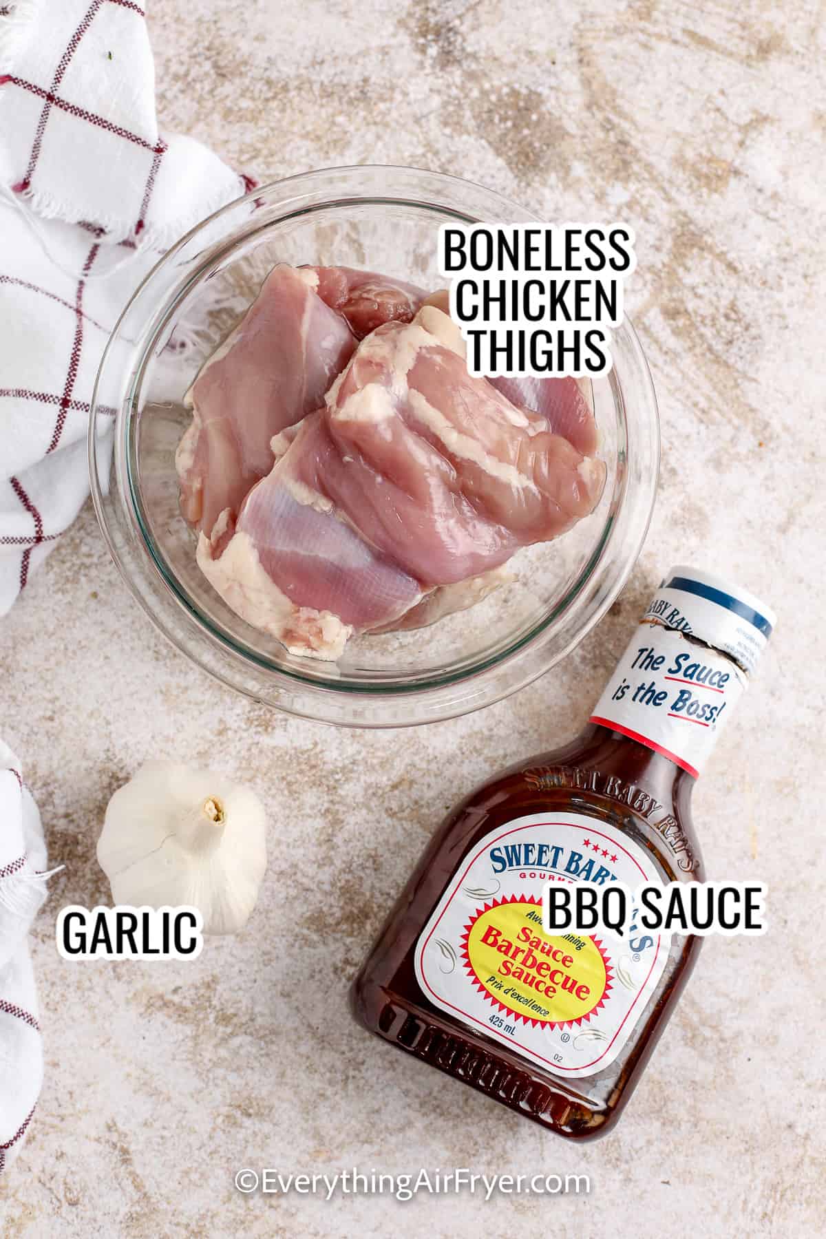 ingredients assembled to make bbq boneless chicken thighs, including chicken thighs, garlic, and bbq sauce