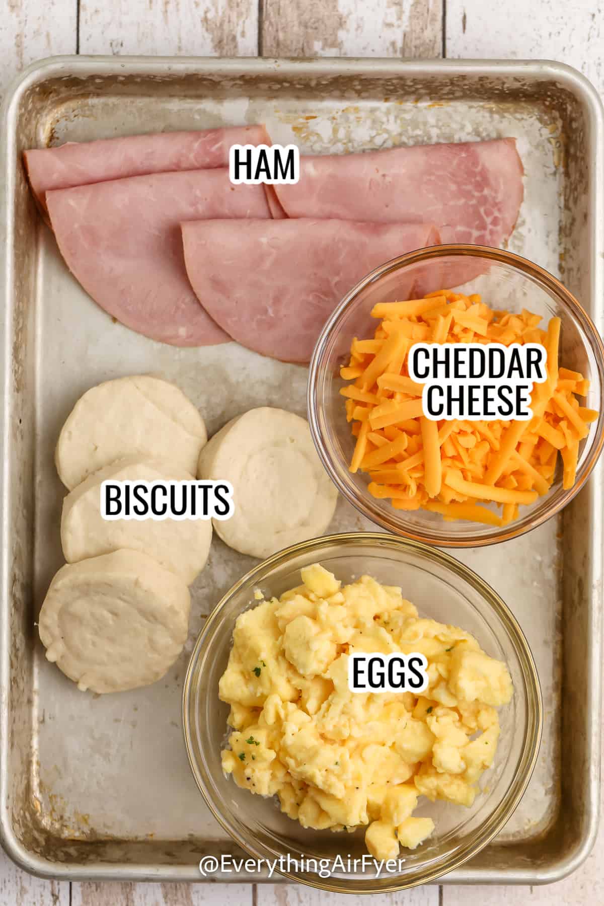 ingredients assembled to make breakfast sandwiches, including biscuits, cheese, ham, and eggs with labels