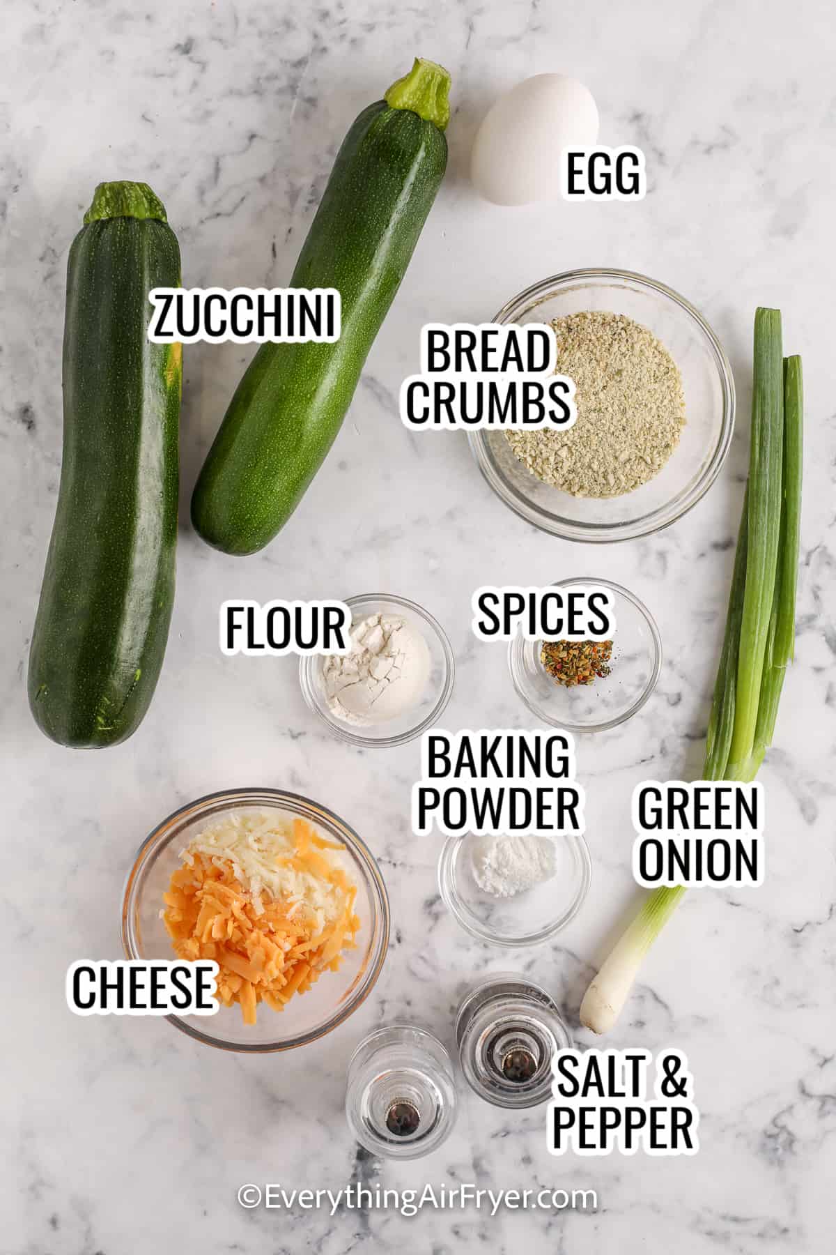 ingredients assembled to make air fryer zucchini fritters including zucchini, green onions, cheese, flour, bread crumbs, and spices