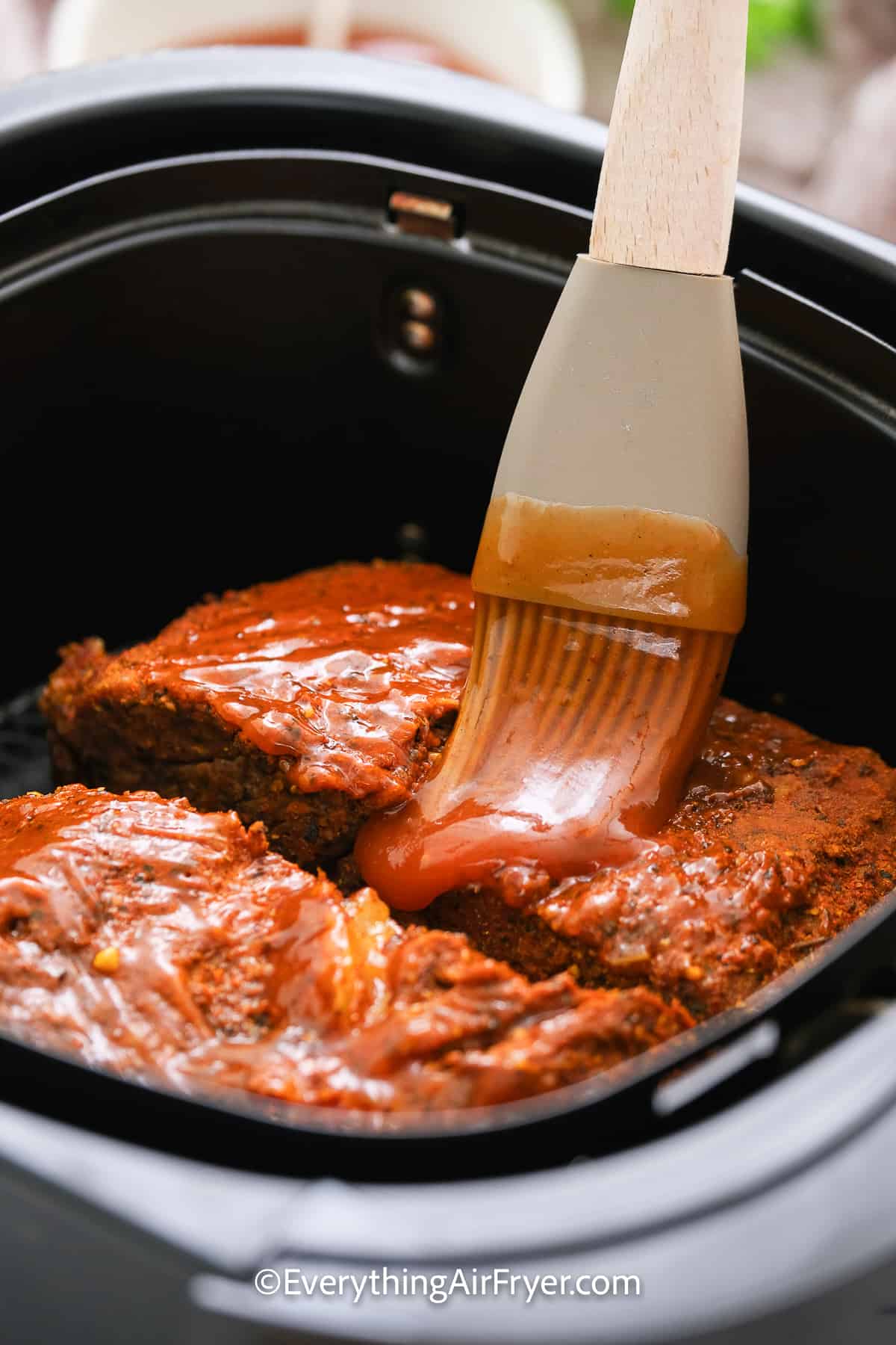 Beef brisket in an air fryer basket being brushed with bbq sauce