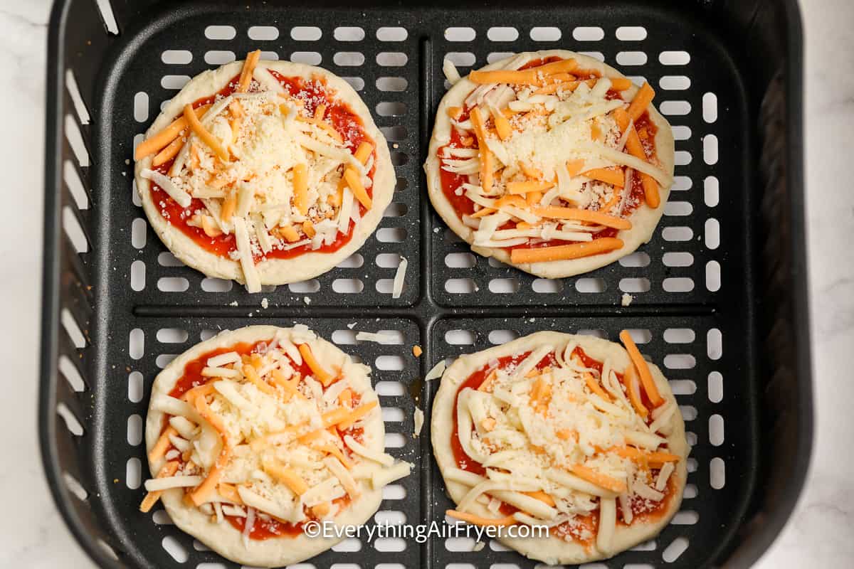 uncooked mini pizzas in an air fryer tray