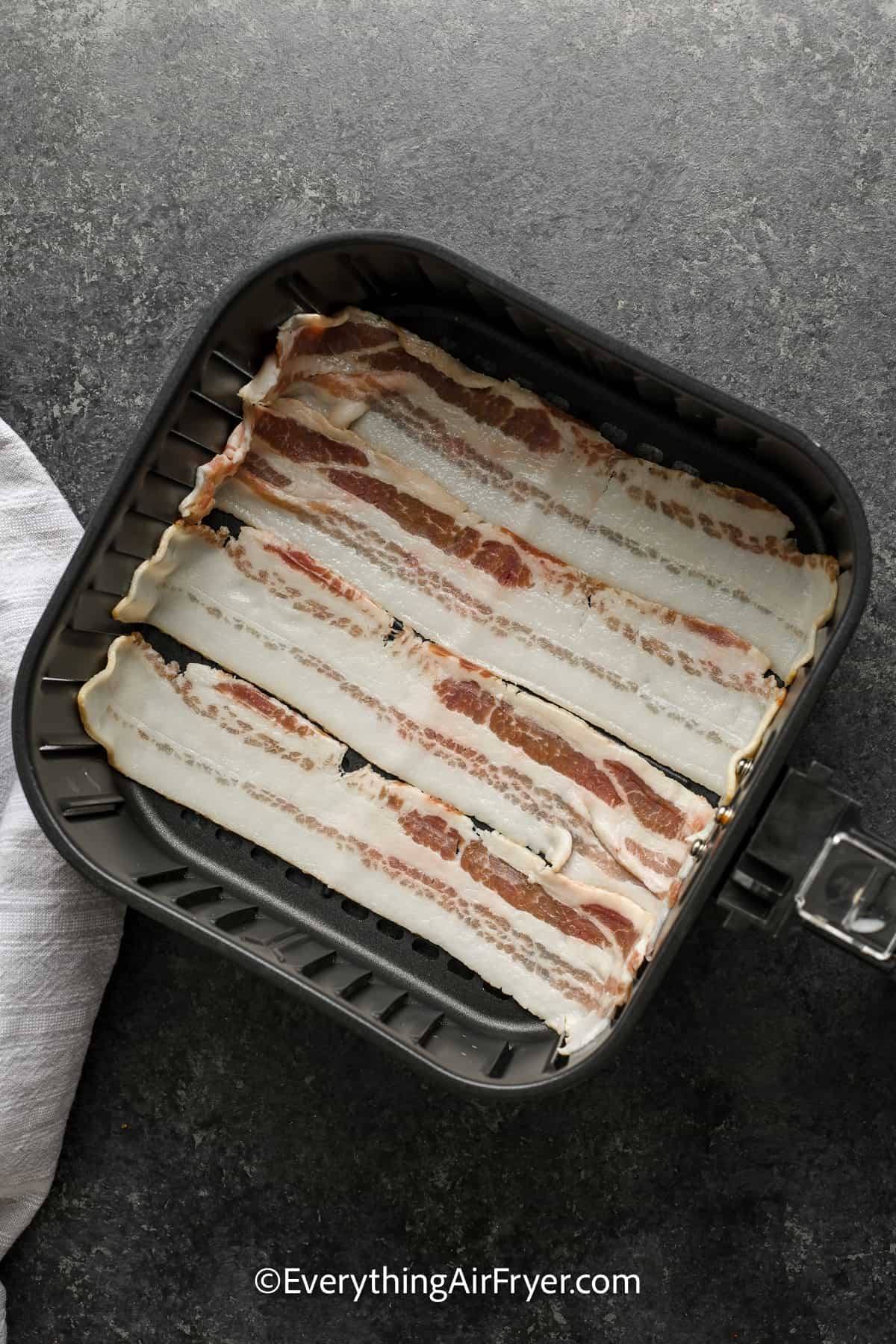 uncooked bacon in an air fryer tray