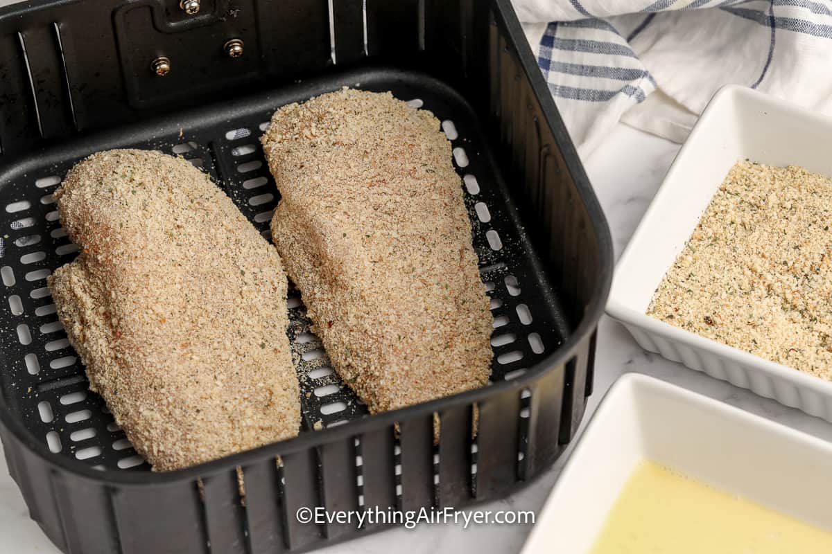 uncooked breaded chicken breasts in an air fryer tray
