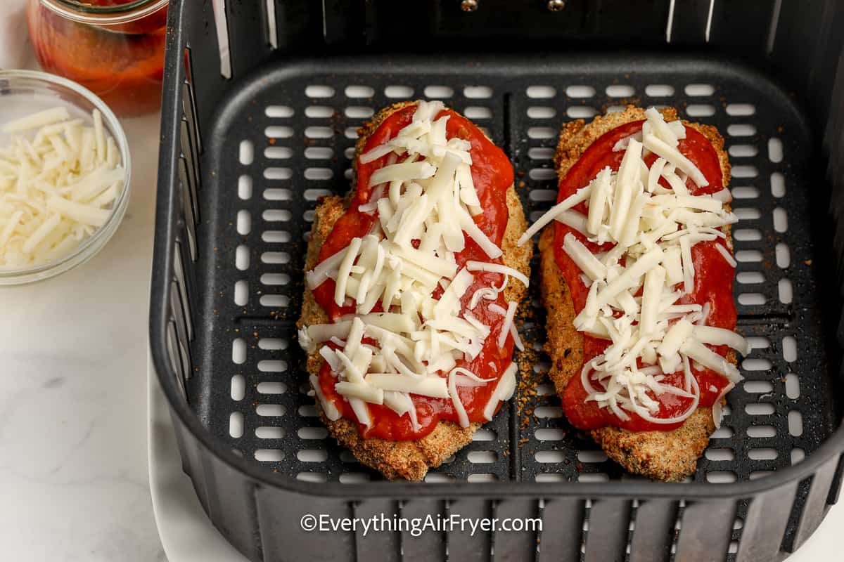 cooked breaded chicken in an air fryer tray topped with marinara sauce and mozzarella cheese