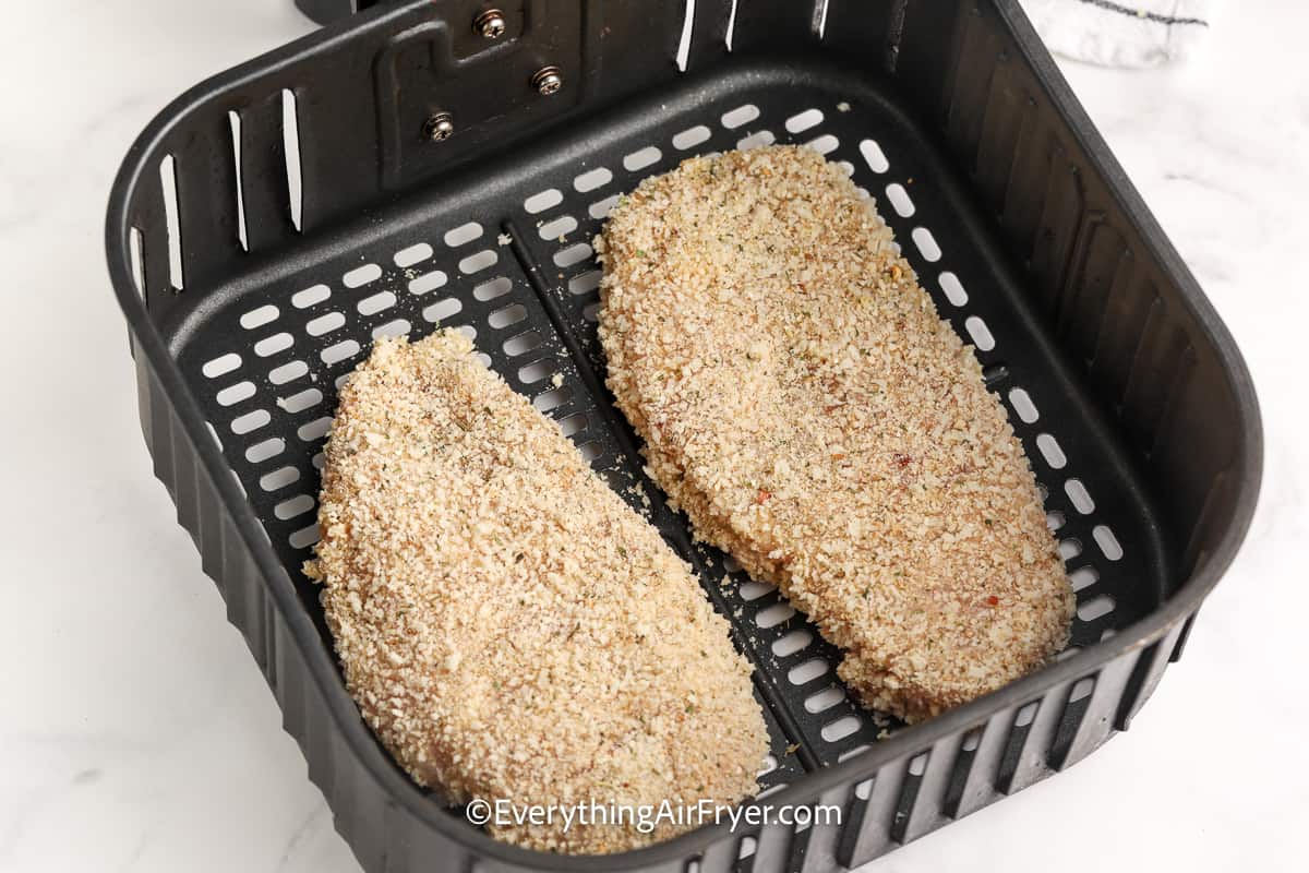 uncooked breaded chicken breasts in an air fryer tray