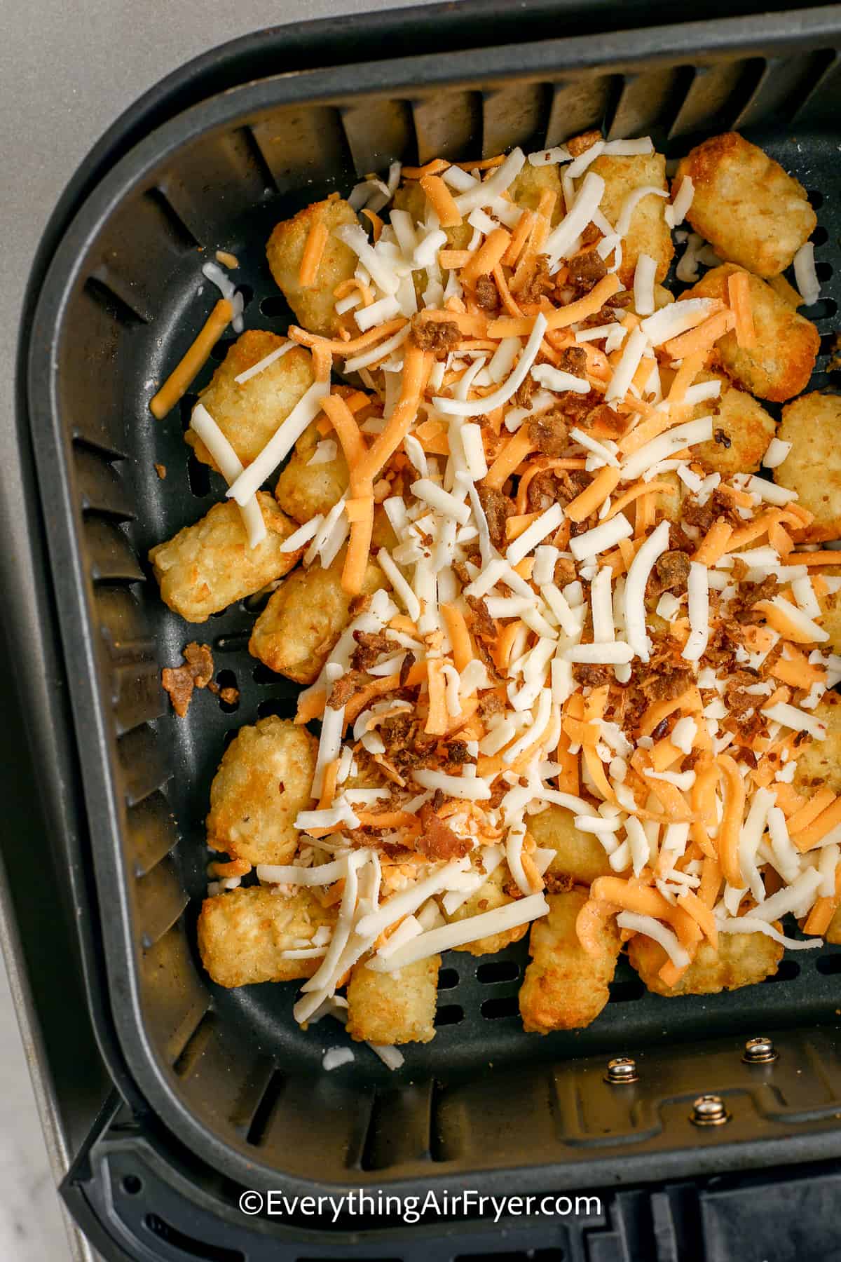 tator tots in an air fryer tray topped with cheese and bacon bits