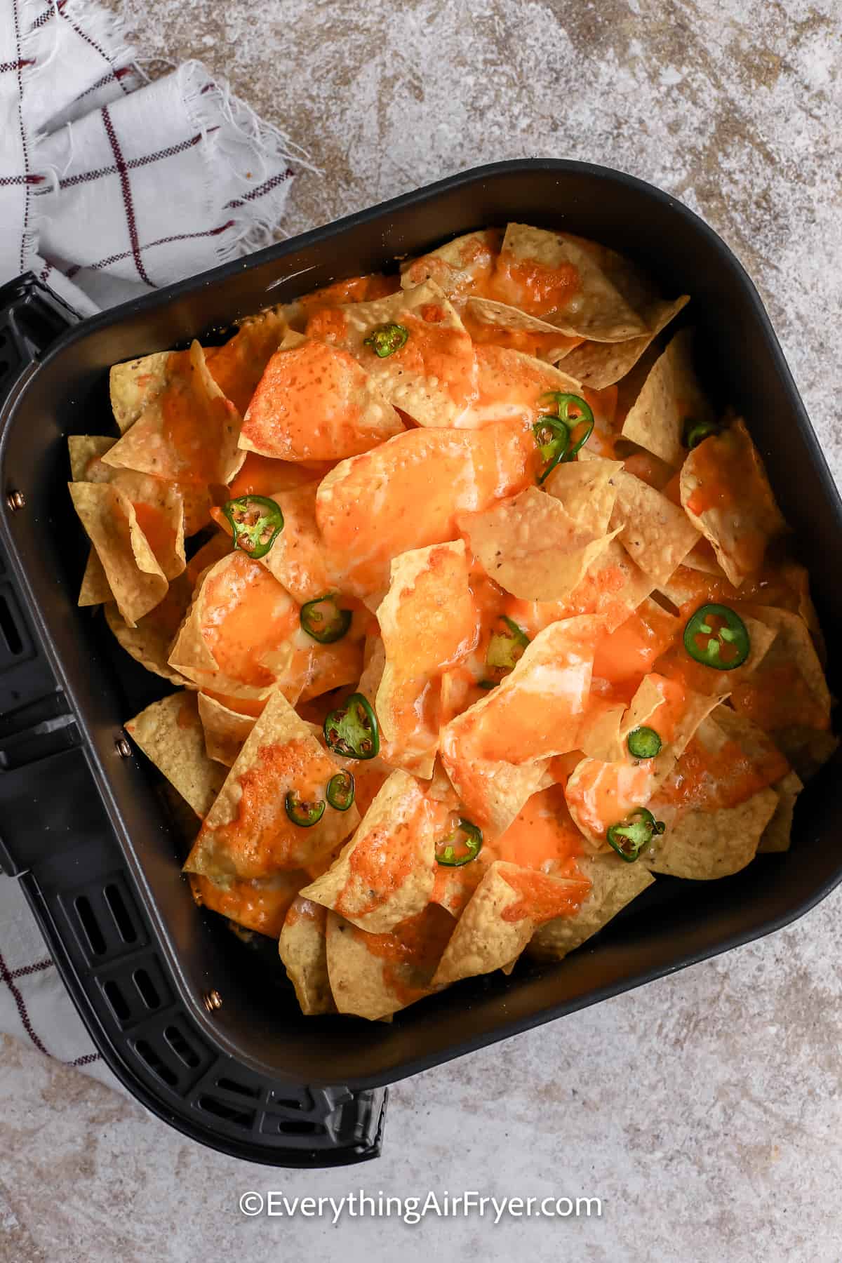cooked nachos topped with cheese and jalapenos in an air fryer tray