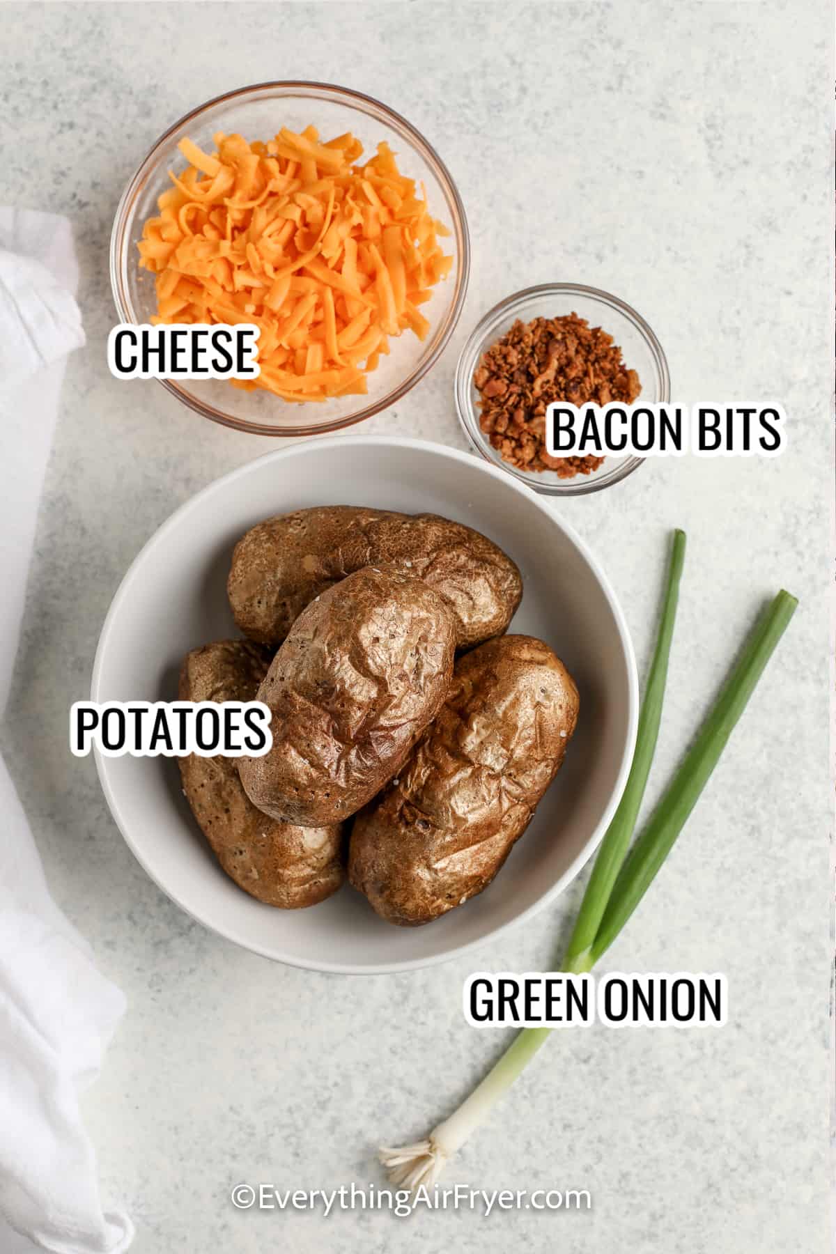 ingredients assembled to make air fryer potato skins, including potatoes, green onions, bacon bits, cheese