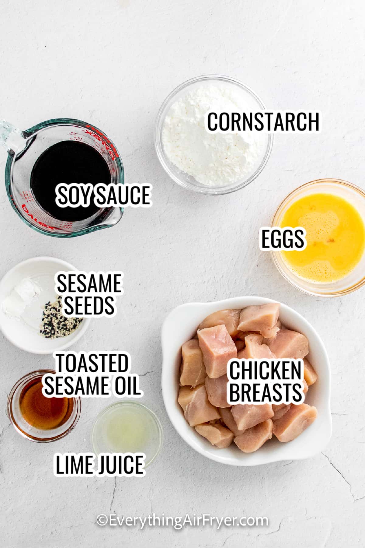 ingredients assembled to make air fryer sesame chicken including soy sauce, cornstarch, eggs, sesame seeds, chicken breast, and lime juice