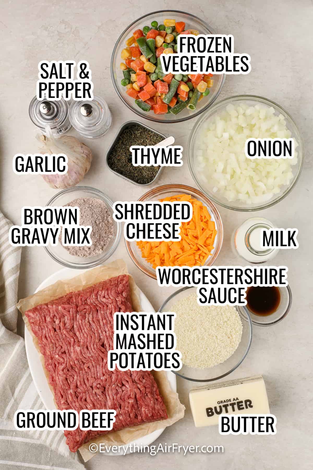 ingredients assembled to make air fryer shepherd's pie, including frozen mixed vegetables, shredded cheese, instant mashed potatoes, ground beef, brown gravy mix, garlic, onion, butter, milk, and worcestershire sauce
