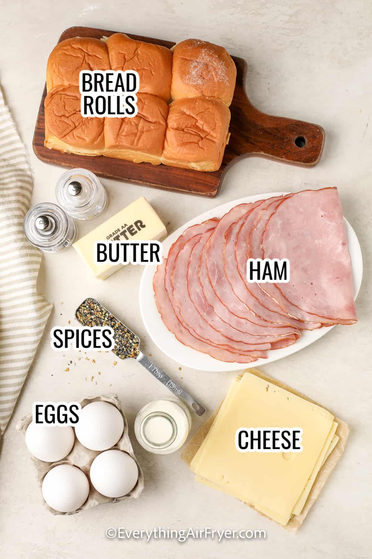 ingredients assembled to make breakfast sliders including bread rolls, butter, ham, eggs, cheese, and spices