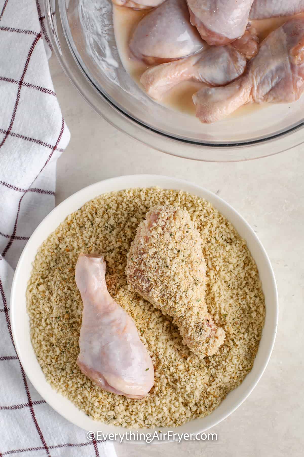 chicken drumsticks being coated with breadcrumbs