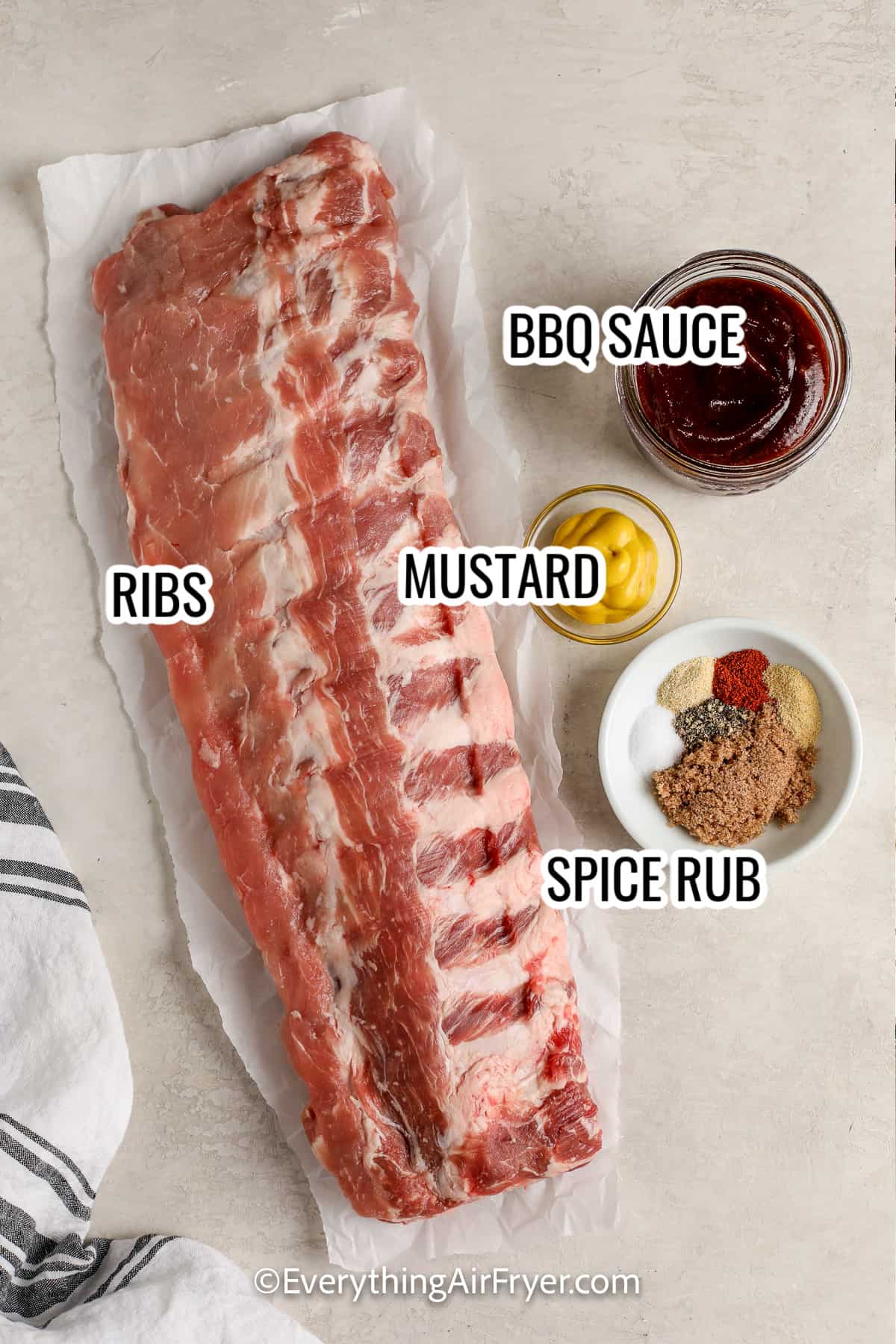 ingredients assembled to make air fryer ribs, including ribs, mustard, bbq sauce, and spices
