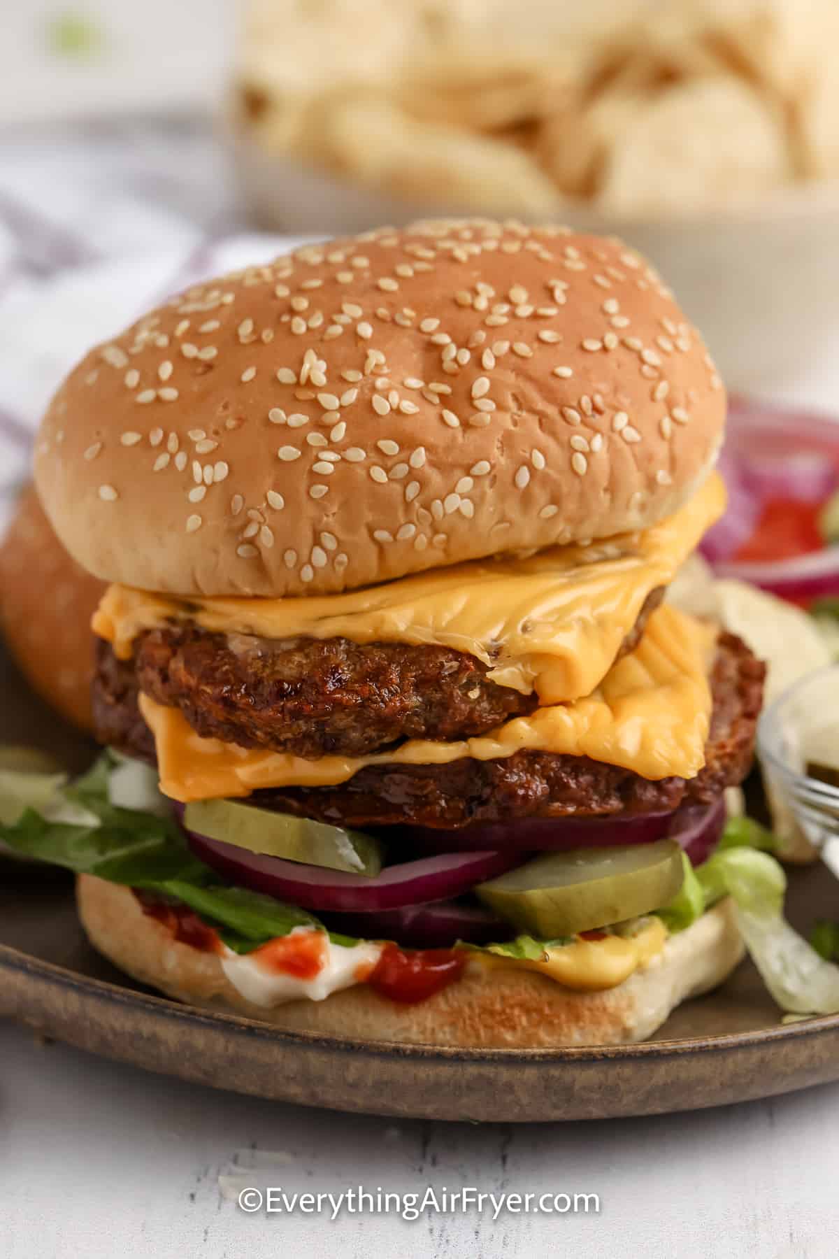 two hamburger patties stacked on a bun with an assortment of condiments