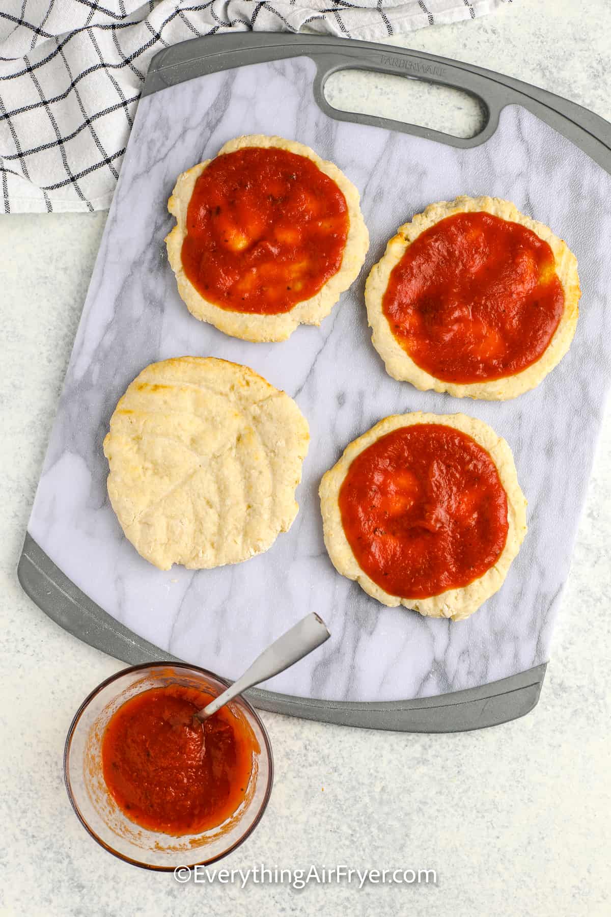 spreading pizza sauce on crusts