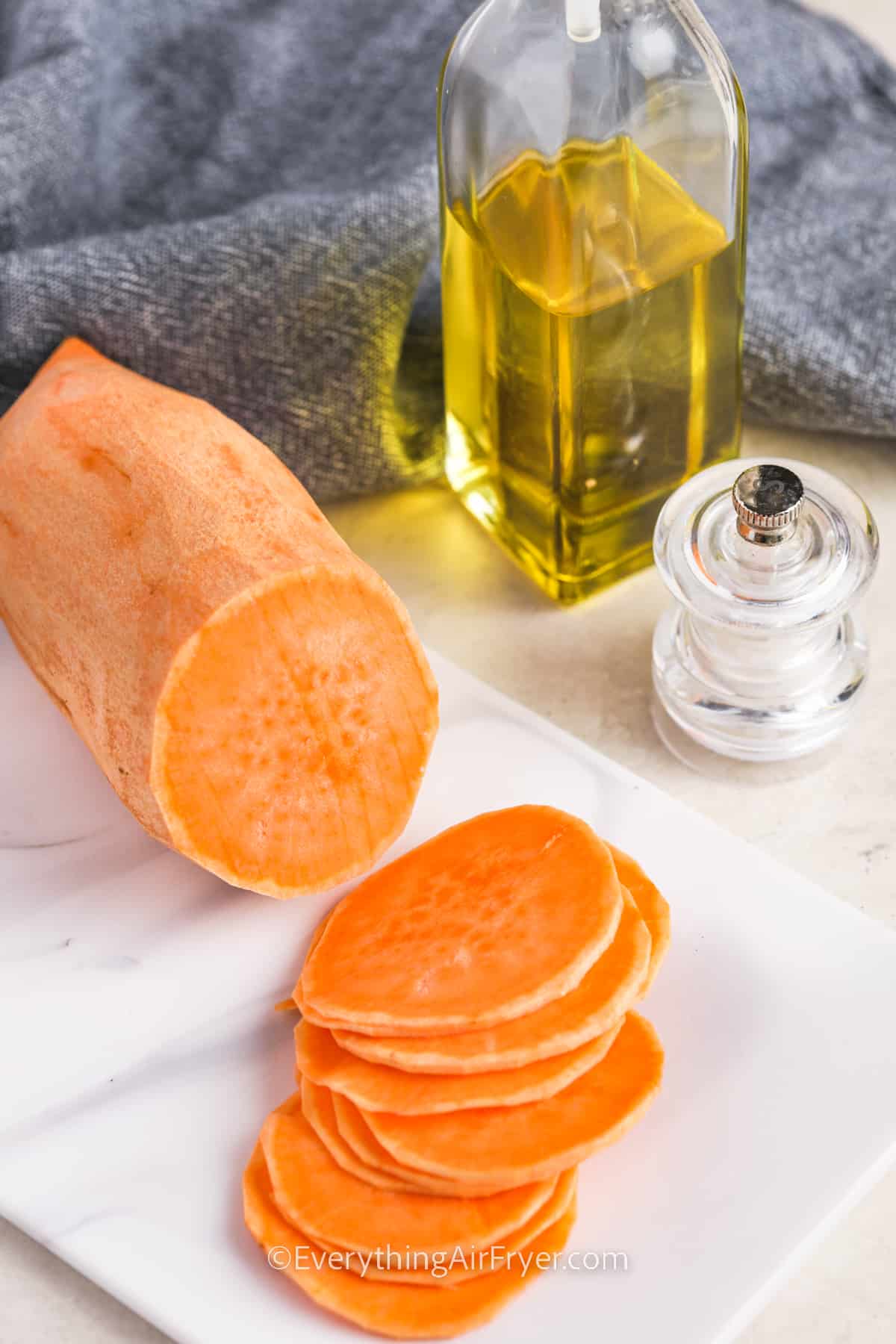 a peeled sweet potato being sliced into rounds on a cutting board to make sweet potato chips