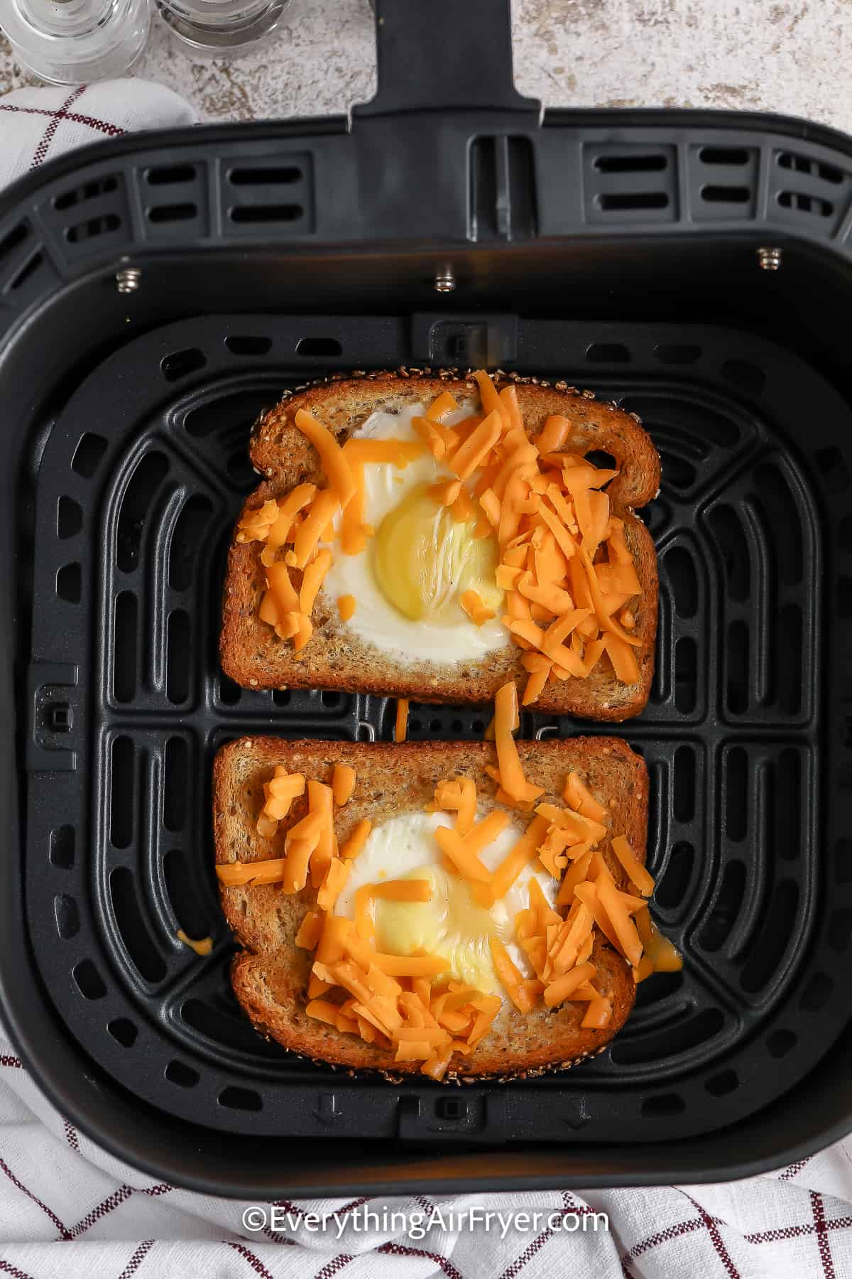 Eggs in a hole sprinkled with cheese in an air fryer basket